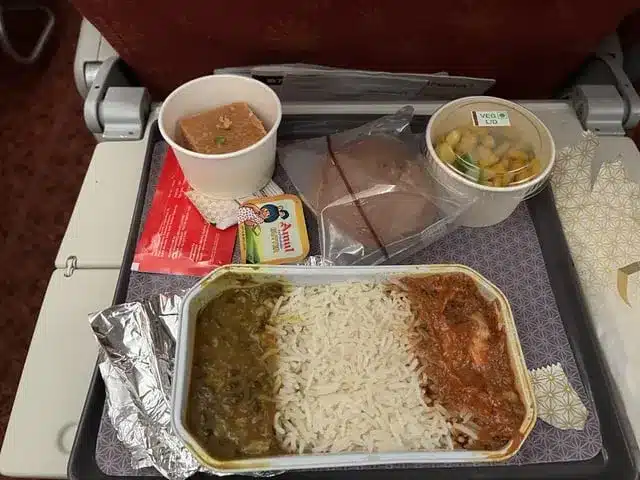 An Image of Air India meals on domestic flights, that includes curry, rice, boiled corn, bread, butter, and a piece of cake